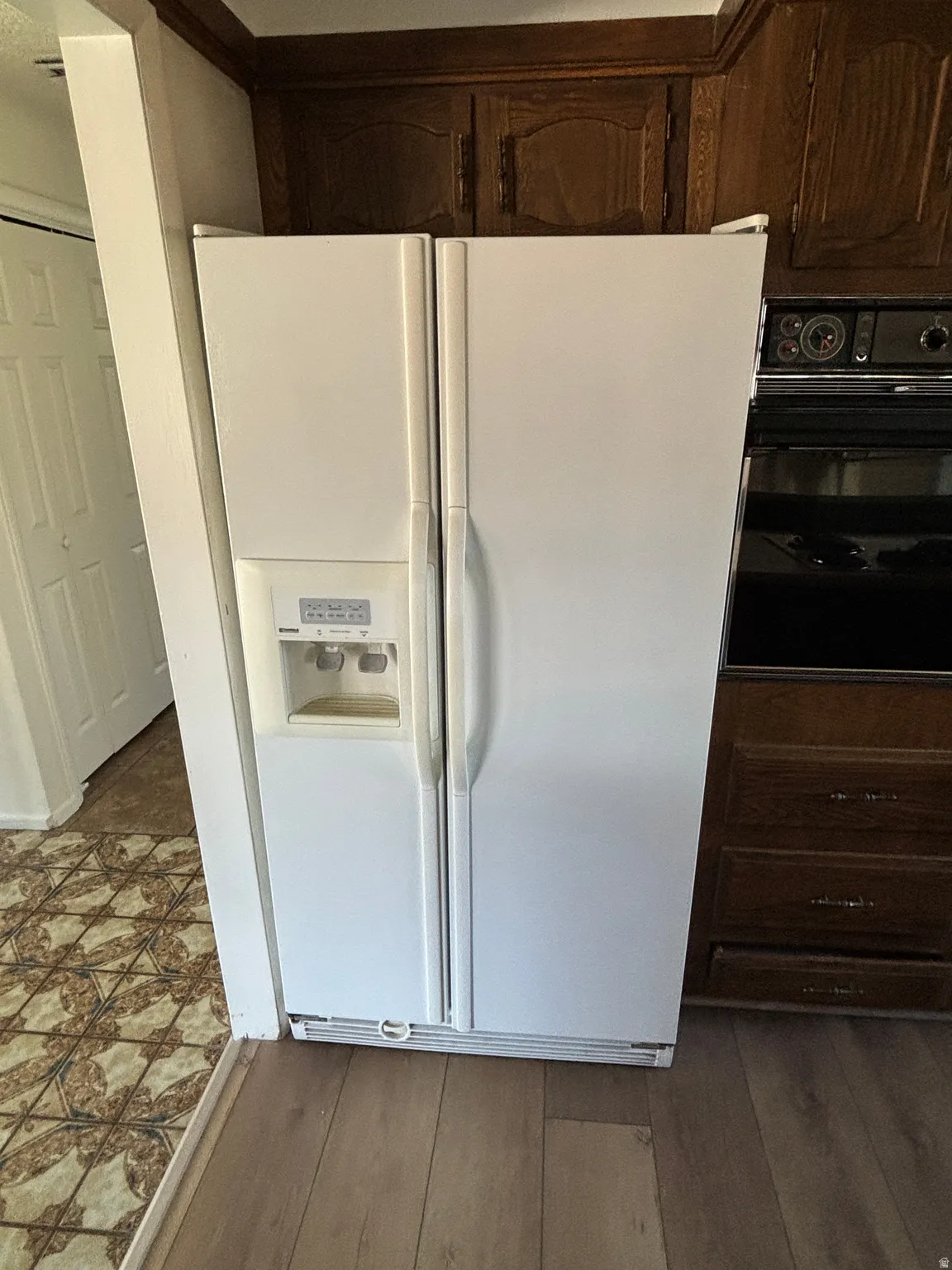 White side-by-side refrigerator, integrated dispenser, dark wood-finish cabinetry, and built-in wall oven