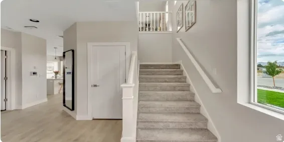 Laminate wood-finish flooring, white paneled doors, carpeted staircase, white railing, and a large window providing natural light.This home is under construction. Pictures are of a similar home.