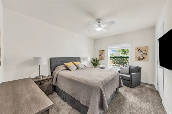 Neutral tone wall paint, textured carpeting, contemporary ceiling fan, window with white trim, and a white door