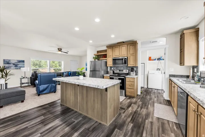 Kitchen featuring wood-finish flooring, light wood cabinetry, a center island with a light-toned countertop, and stainless steel appliances