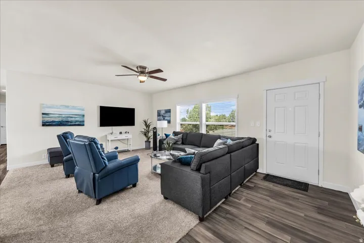 Spacious living area featuring a ceiling fan, wood-finish flooring, and ample natural light through large windows