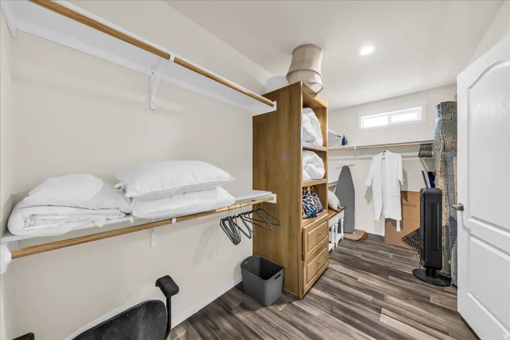 Walk-in closet featuring wood-finish flooring, built-in shelving, hanging rods, and a window for natural light