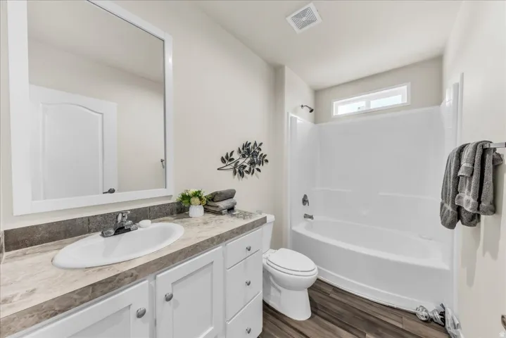 Bathroom featuring a single vanity with an integrated sink, a rectangular mirror, a white two-piece toilet, a tub/shower combination, and wood-finish flooring