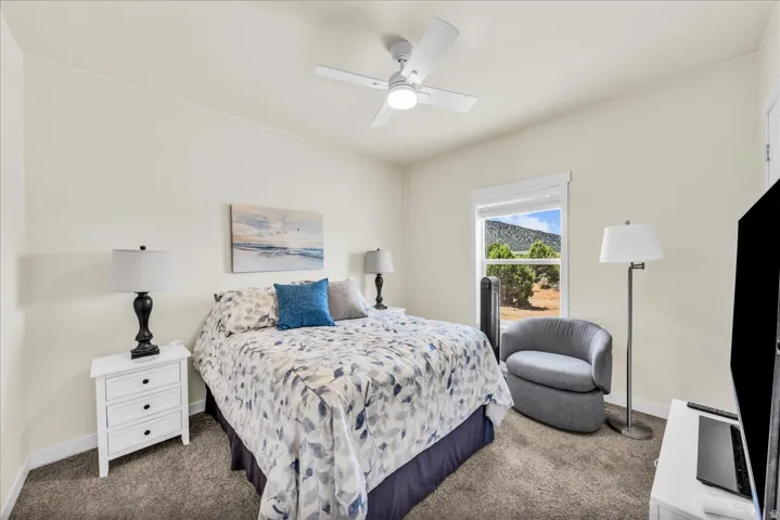 Ceiling fan light fixture, light-toned wall paint, carpeted flooring, window with white trim, and a mountain backdrop