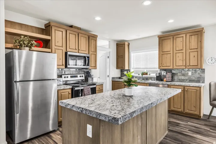 Kitchen featuring wood-finish cabinetry, stainless steel appliances, a center island with a stone-finish countertop, recessed lighting, and wood-finish flooring