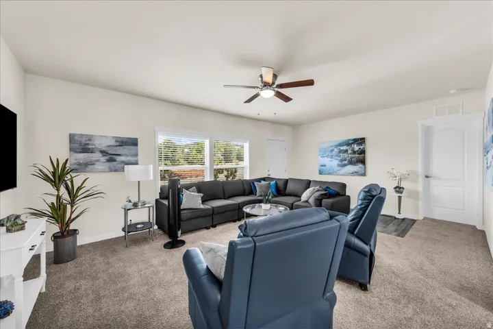 Spacious living area featuring neutral walls, carpeting, multiple windows, a ceiling fan, and white interior doors