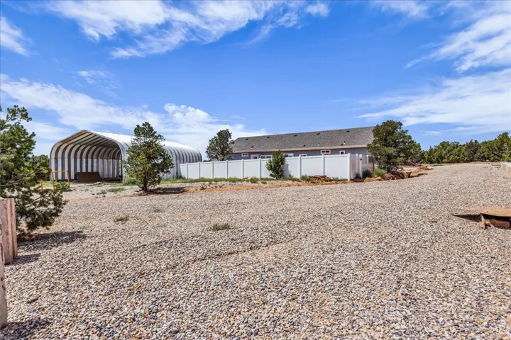 Expansive gravel lot featuring a large arched storage structure and a white privacy fence