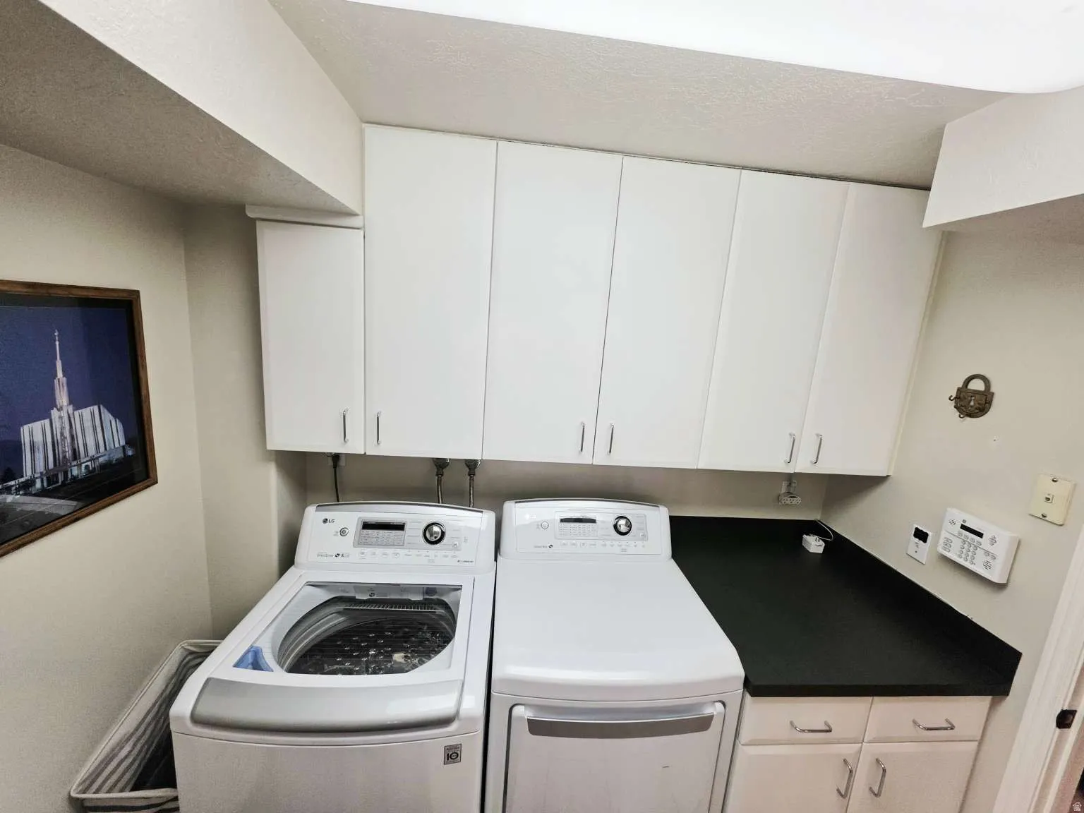 White upper cabinetry, white lower cabinetry, dark countertop, and overhead lighting