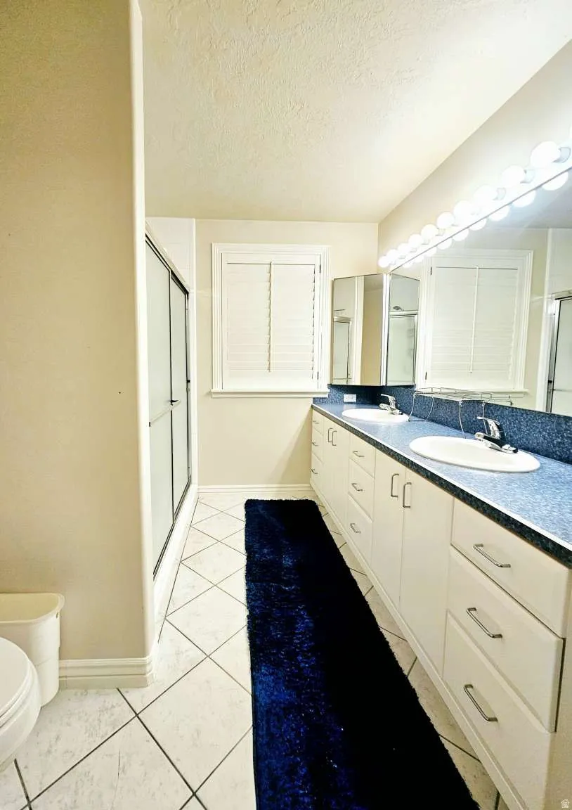Dual vanity with integrated sinks, white cabinetry with silver-tone hardware, and a framed mirror with vanity lighting