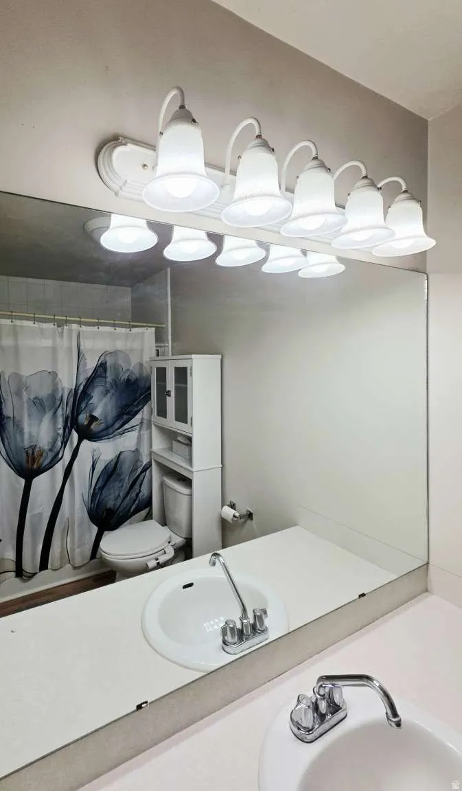 Extended vanity with two integrated sinks, chrome fixtures, and overhead multi-bulb lighting