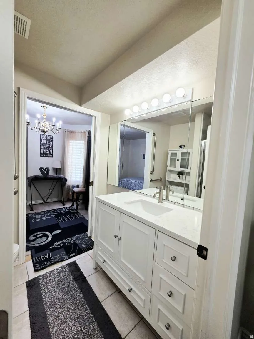 White vanity with an integrated sink and brushed nickel faucet, large wall-mounted mirror, and tile flooring