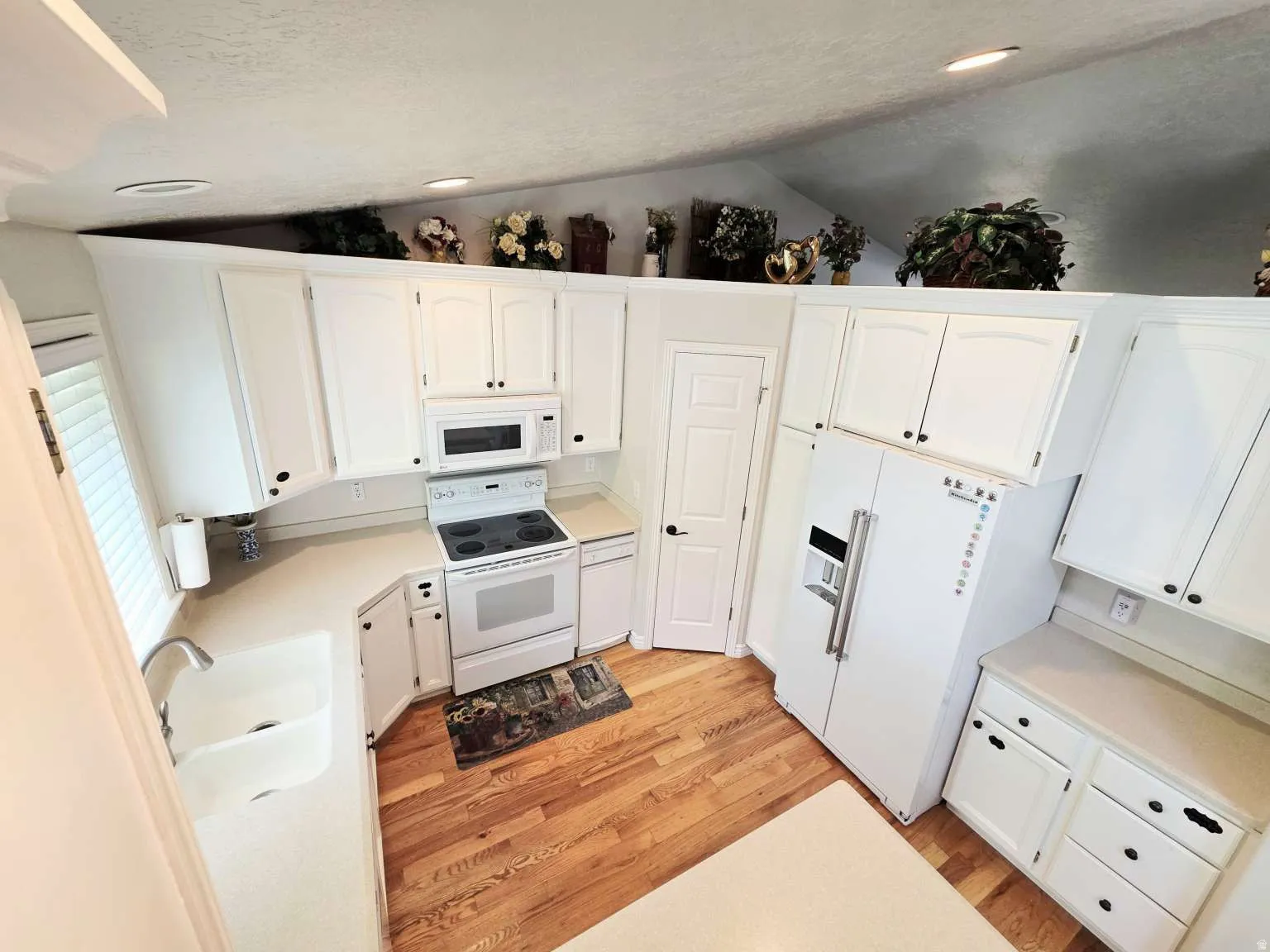 White cabinetry with dark hardware, light-toned countertops, and wood-finish flooring