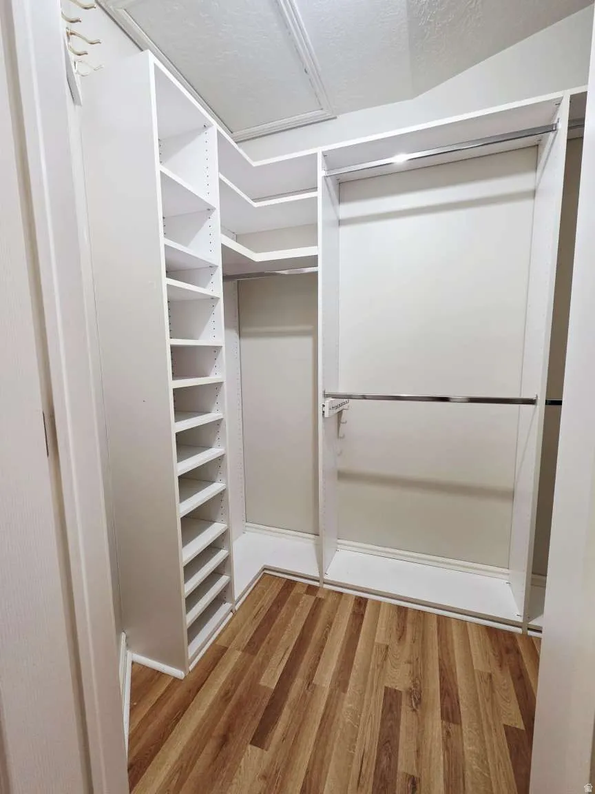 Built-in closet system featuring white shelving, multiple hanging rods, and wood-finish flooring
