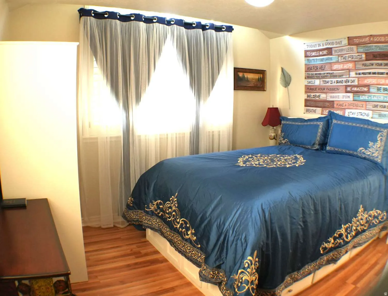 Wood-finish flooring with a light tone, ceiling-mounted light fixture, and window with sheer and solid curtains