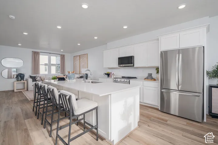 White shaker cabinetry, stainless steel appliances, wood-finish flooring, recessed lighting, and a kitchen island with seating