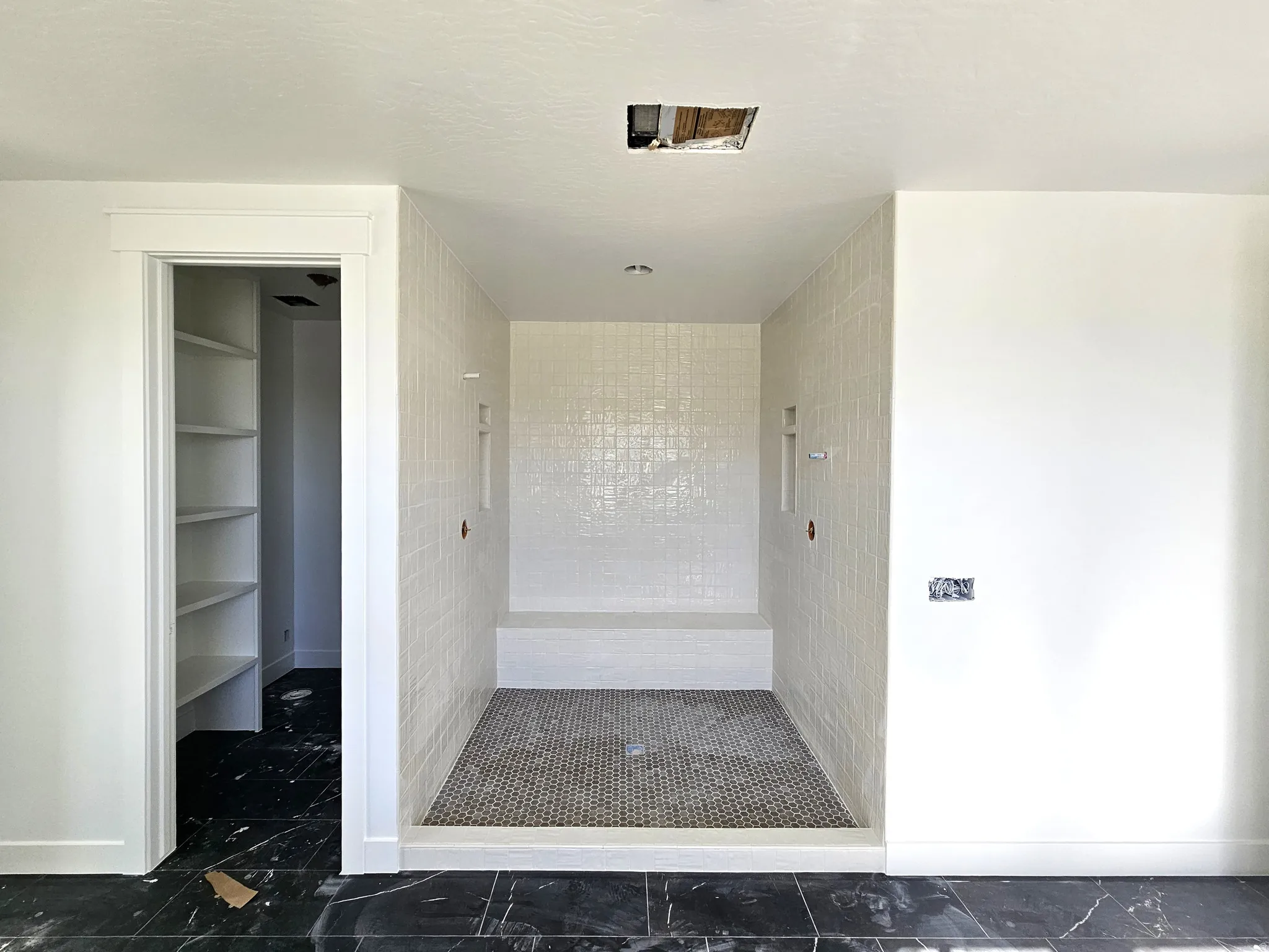 Walk-in shower with a tiled bench and integrated niches, complemented by a black and white tiled floor