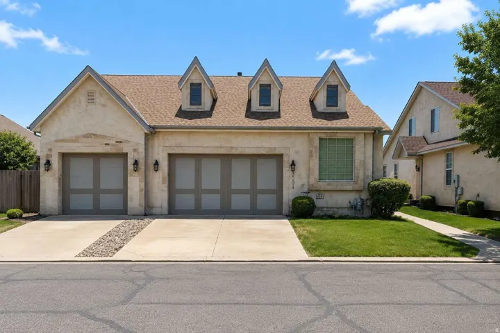 Stucco exterior featuring multiple dormer windows, a two-car garage, a single-car garage, and a concrete driveway with a central rock accent