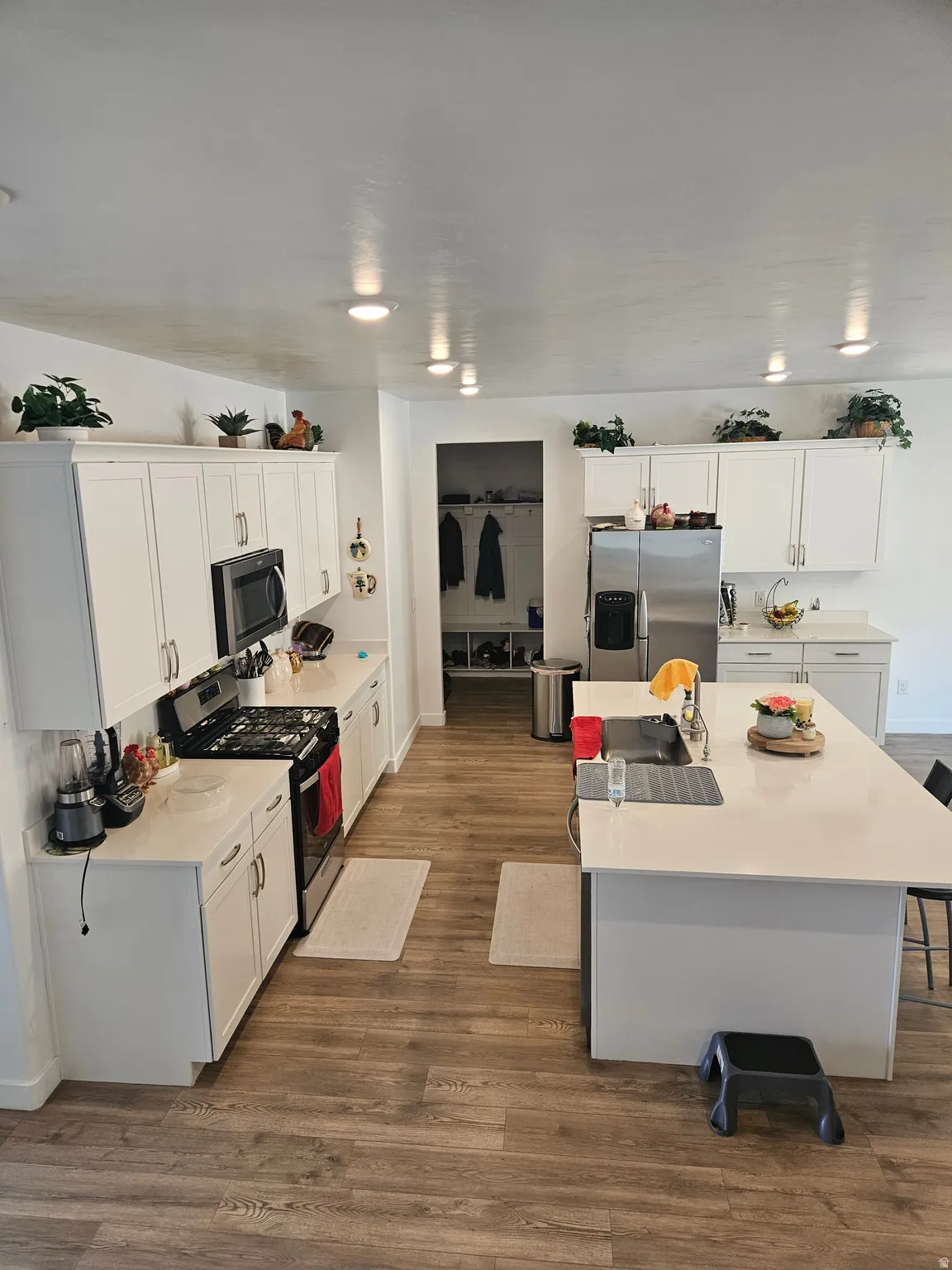 Kitchen featuring wood-finish flooring, white cabinetry, a kitchen island with seating, recessed lighting, and stainless steel appliances