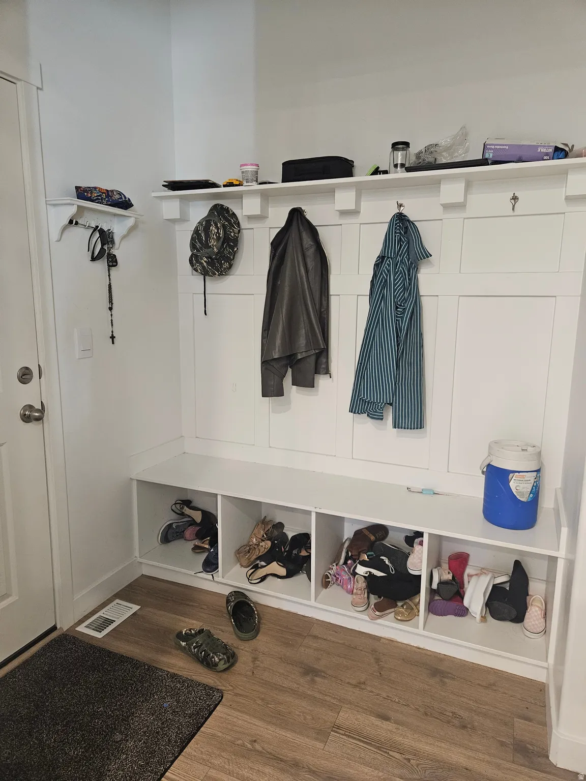 Built-in entryway storage with hooks, an integrated bench, and dedicated shoe cubbies, featuring wood-finish flooring