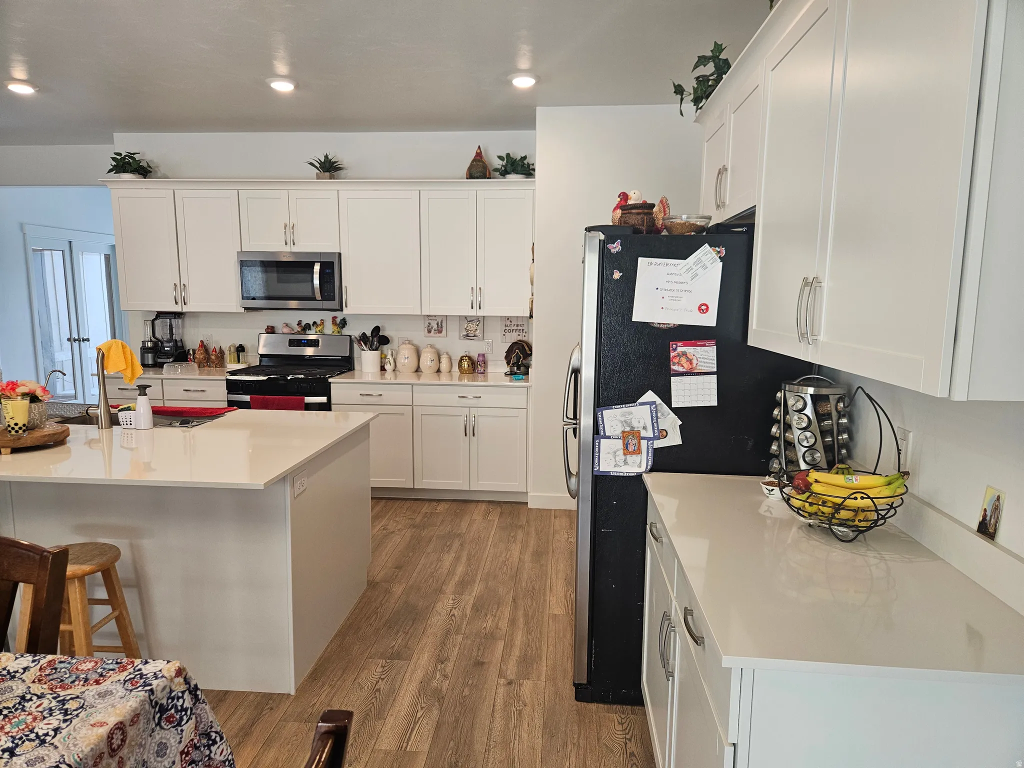 Kitchen featuring white shaker-style cabinetry, light-toned countertops, stainless steel appliances, a center island with a sink, and wood-finish flooring