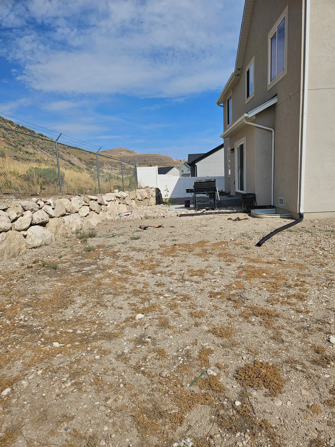 Rear exterior featuring a sliding glass door, a stone retaining wall, and a chain-link fence