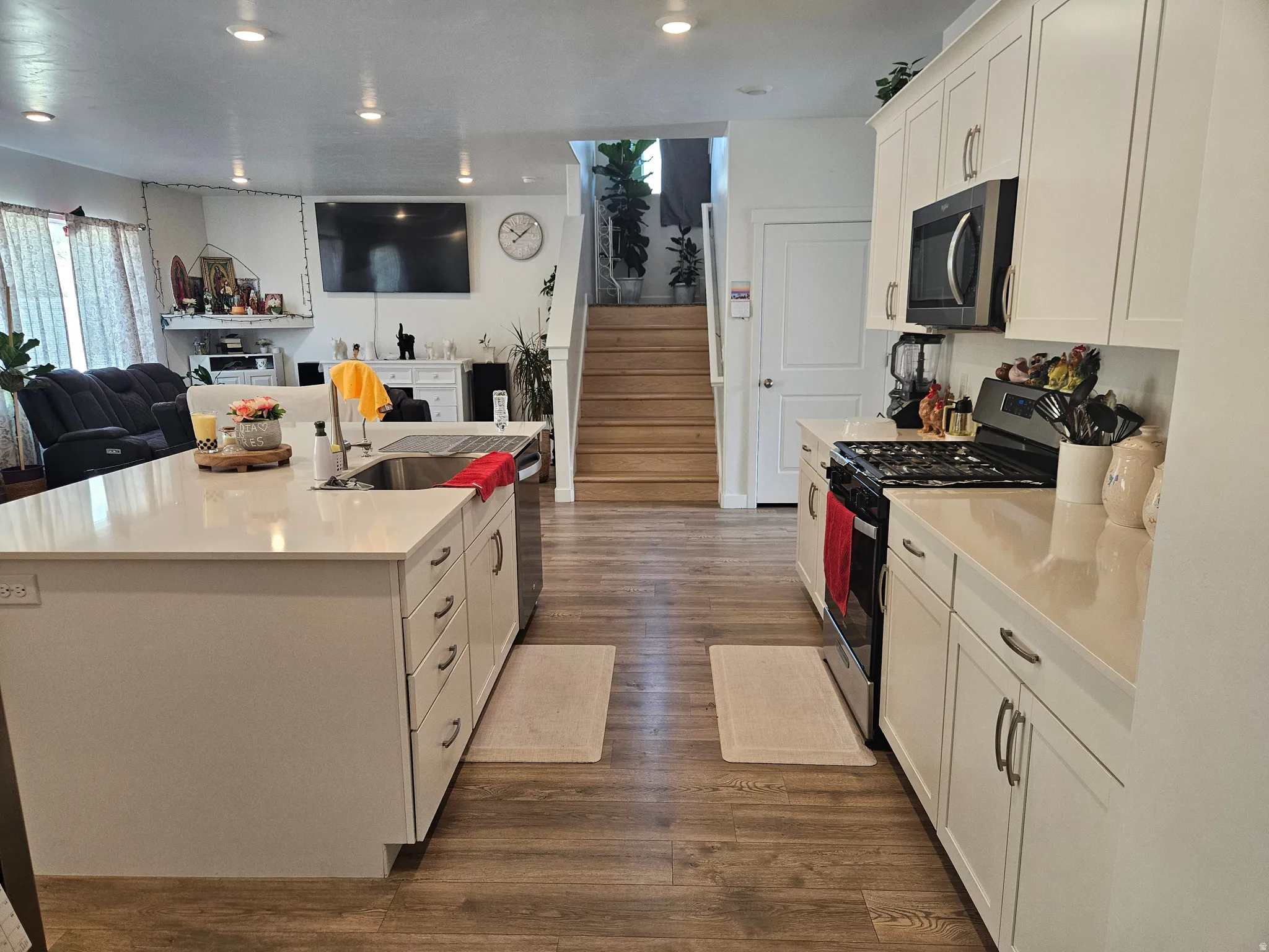 Open-concept living area with wood-finish flooring, white cabinetry, quartz countertops, a kitchen island with an undermount sink, and recessed lighting