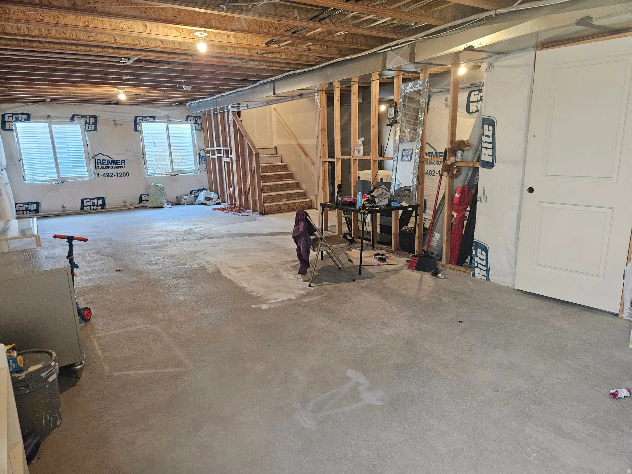 Unfinished basement with exposed ceiling joists, concrete flooring, framed interior walls, and visible windows