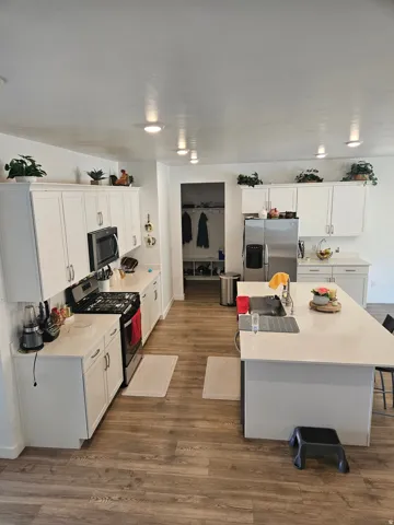 Kitchen featuring wood-finish flooring, white cabinetry, a kitchen island with seating, recessed lighting, and stainless steel appliances