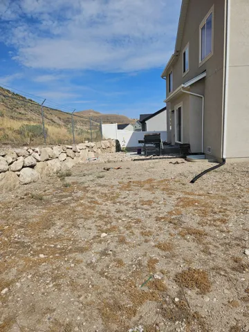 Rear exterior featuring a sliding glass door, a stone retaining wall, and a chain-link fence