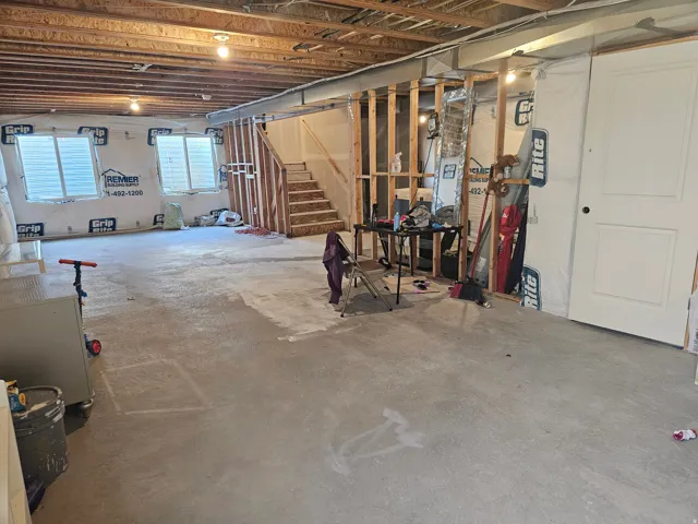 Unfinished basement with exposed ceiling joists, concrete flooring, framed interior walls, and visible windows