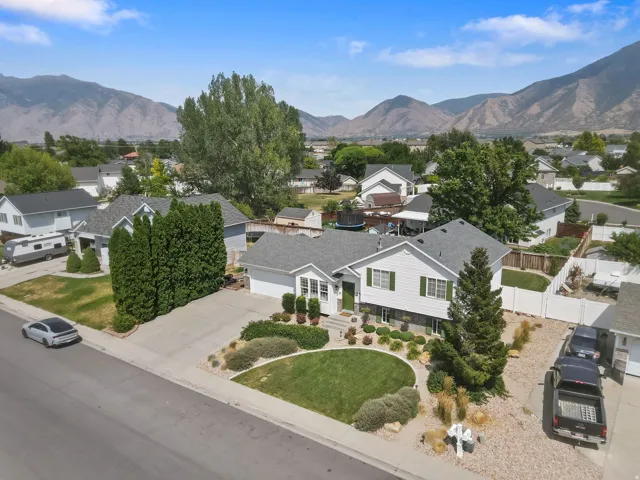 White exterior with green shutters, attached garage, well-maintained front lawn, mature landscaping, and mountain backdrop