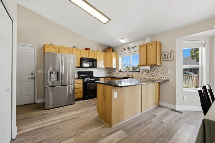 Modern kitchen featuring stainless steel French-door refrigerator and black appliances, wood-finish cabinetry with ample storage, granite countertops, mosaic tile backsplash, and a spacious island with seating