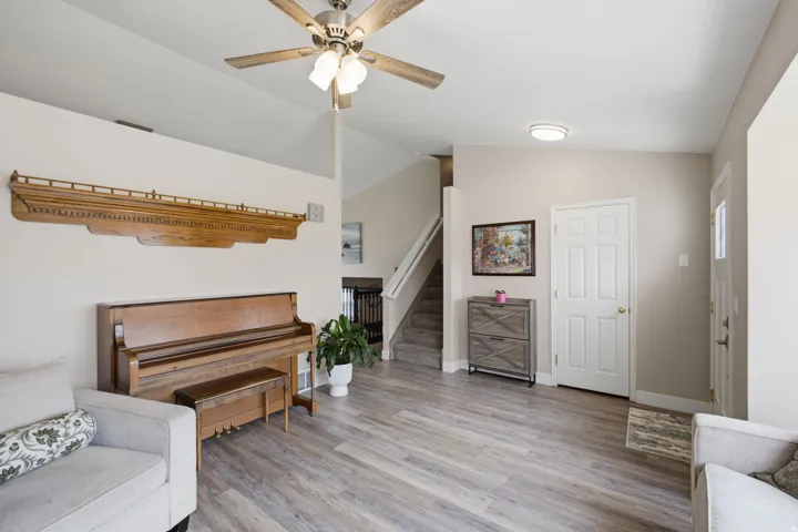Vaulted ceiling with a ceiling fan, light wood-finish flooring, staircase with carpeted treads, and a white six-panel door