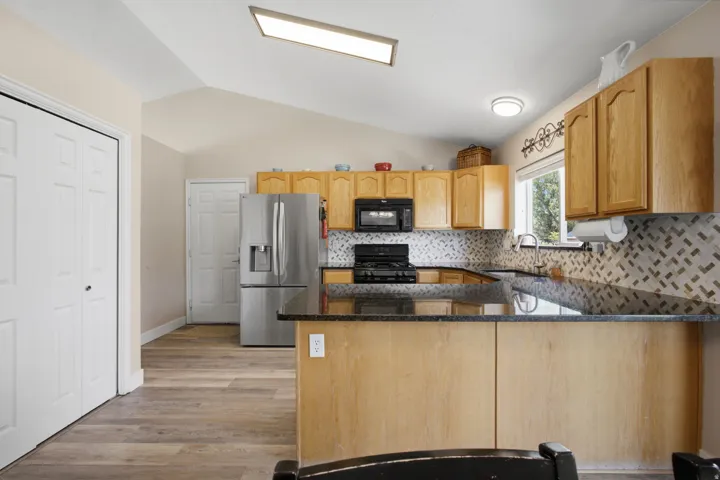 Kitchen featuring wood-finish flooring, vaulted ceilings, natural wood cabinetry, dark countertops, and a mosaic tile backsplash