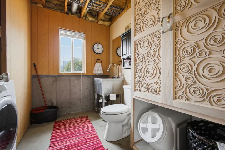 Functional bathroom featuring wood-finish cabinetry, a ceramic toilet, pedestal sink, and decorative wall paneling with circular motif detailing