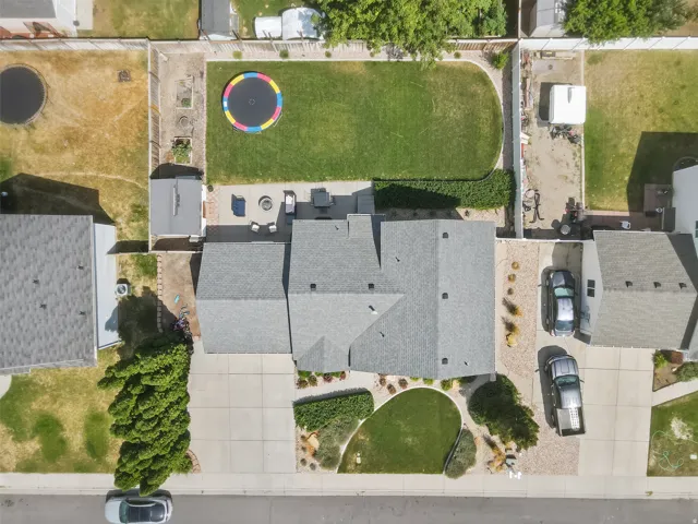 Asphalt shingle roof, expansive concrete driveway, detached shed, paved patio, and a manicured lawn