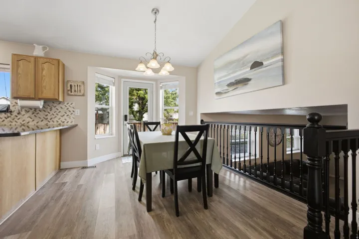 Wood-finish flooring, bay window, light wood cabinetry, tiled backsplash, and black railing