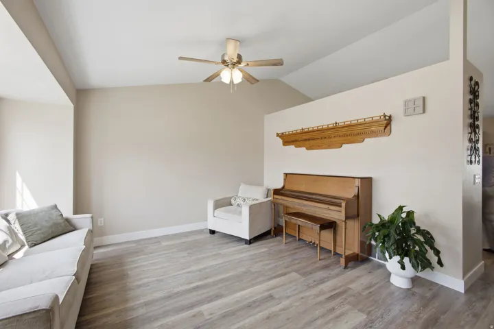 Vaulted ceilings, wood-finish flooring, neutral wall tones, white trim, and a ceiling fan with integrated lighting