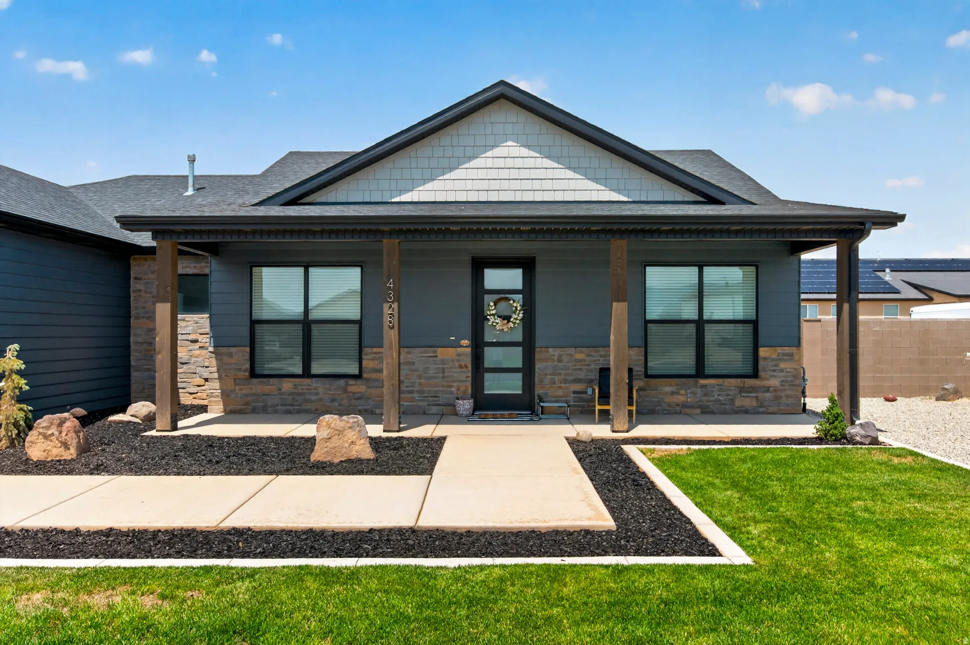 Contemporary exterior featuring dark siding, stone veneer accents, wood posts, a covered entry, and dark-framed windows