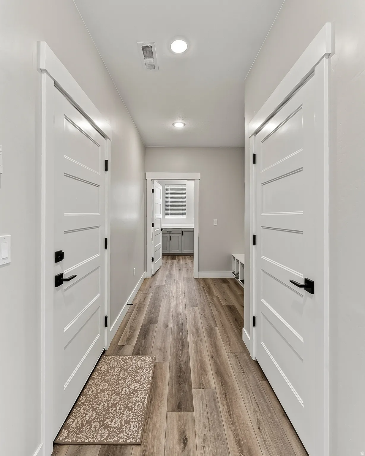 Hallway with wood-finish flooring, recessed lighting, white paneled doors, and black door hardware