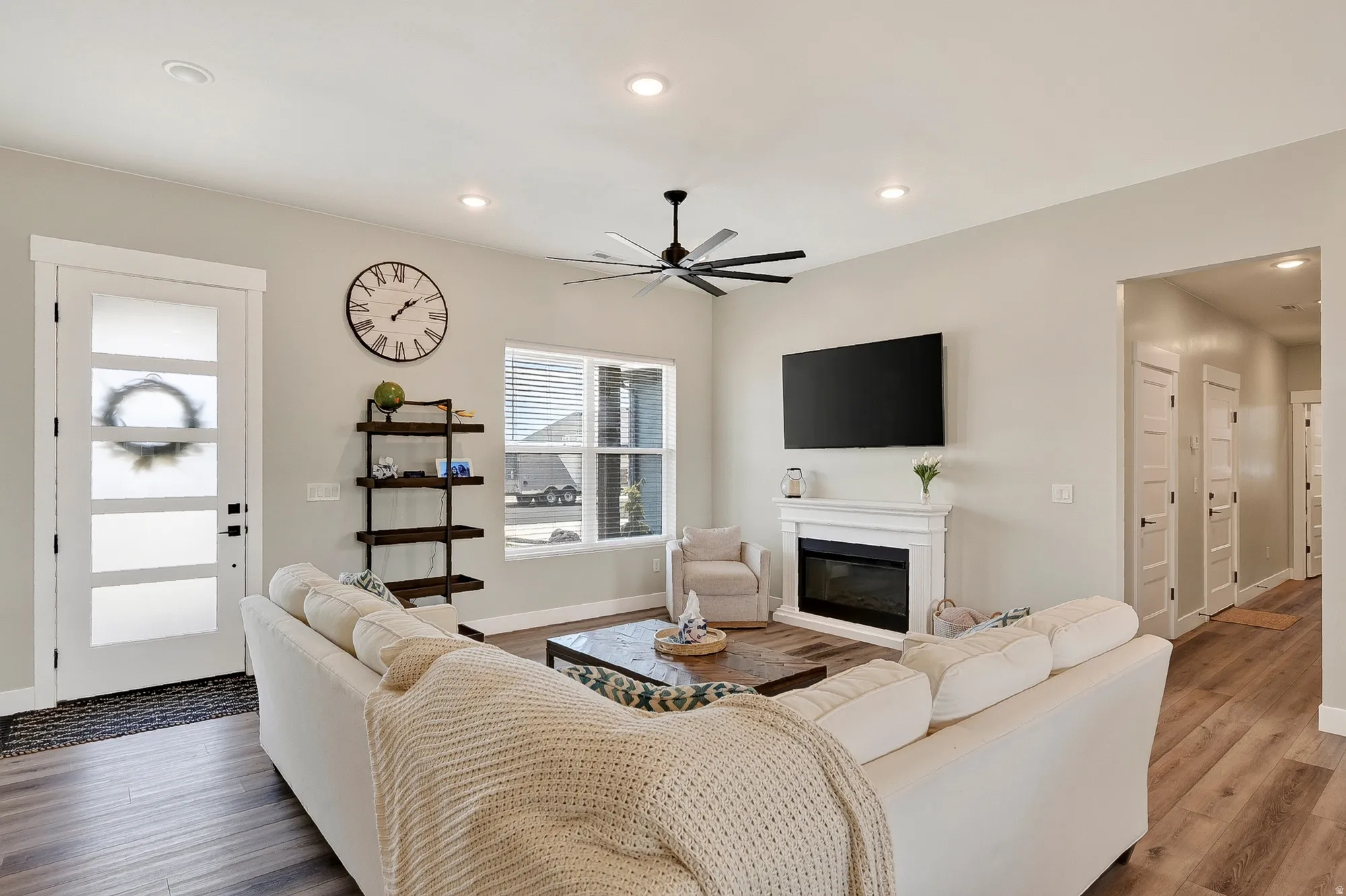 Spacious living area featuring wood-finish flooring, a white mantel fireplace, ceiling fan, and recessed lighting