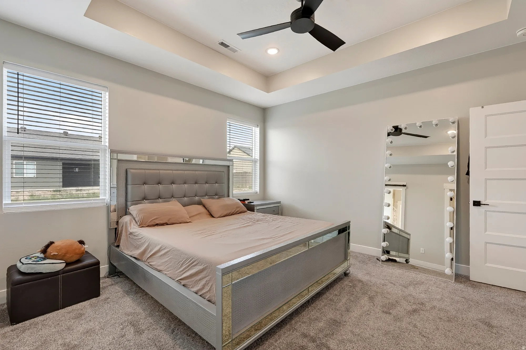 Recessed lighting, ceiling fan, tray ceiling, two windows with blinds, and light gray wall paint