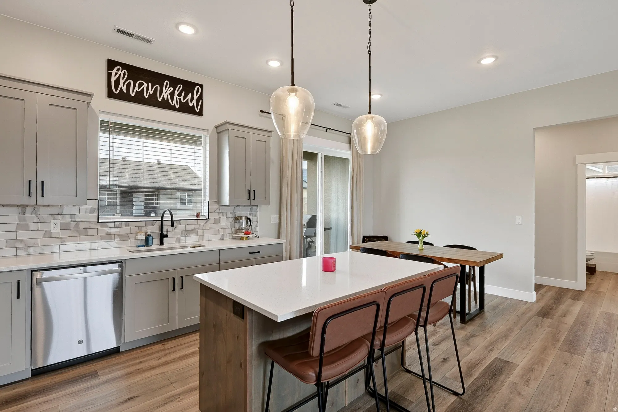 Kitchen featuring gray cabinetry, white countertops, tile backsplash, stainless steel appliances, and wood-finish flooring