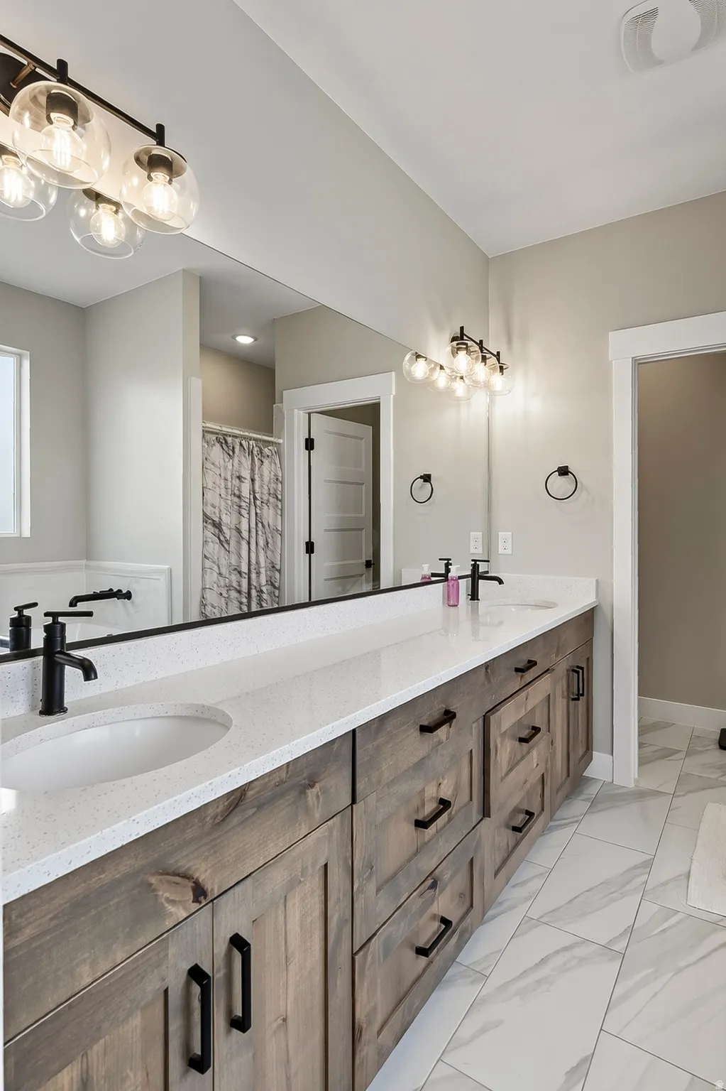 Dual vanity with wood-finish cabinetry, quartz countertops, and matte black fixtures
