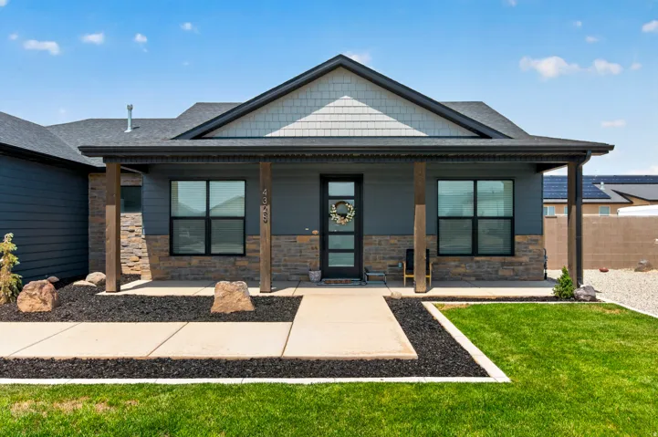 Contemporary exterior featuring dark siding, stone veneer accents, wood posts, a covered entry, and dark-framed windows