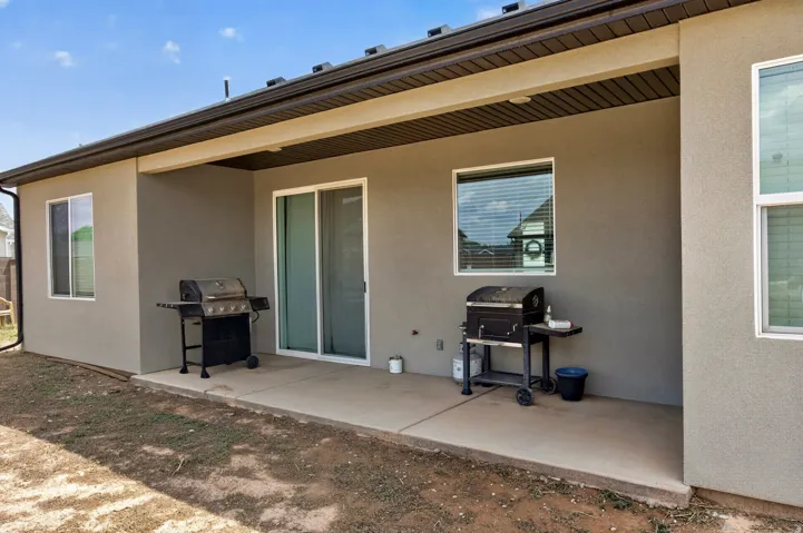 Rear patio with stucco exterior, sliding glass door, and multiple windows