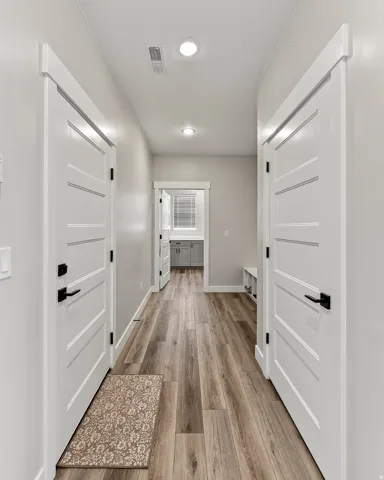 Hallway with wood-finish flooring, recessed lighting, white paneled doors, and black door hardware