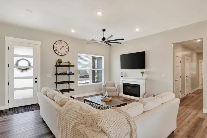 Spacious living area featuring wood-finish flooring, a white mantel fireplace, ceiling fan, and recessed lighting