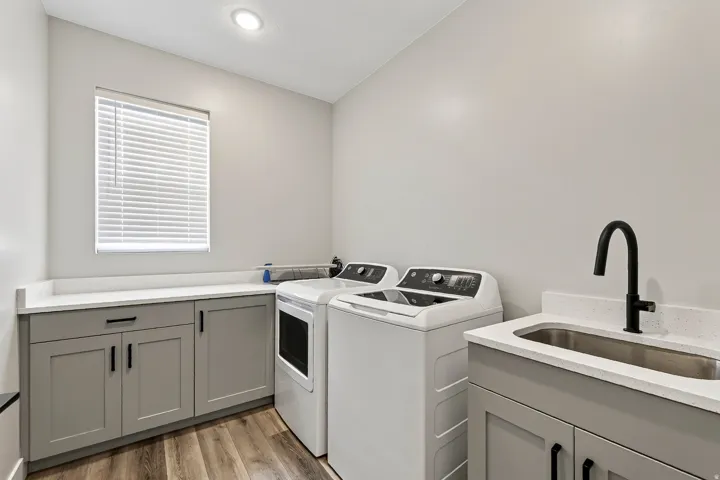 Laundry room featuring wood-finish flooring, light gray cabinetry, white countertops, and a utility sink with a matte black faucet