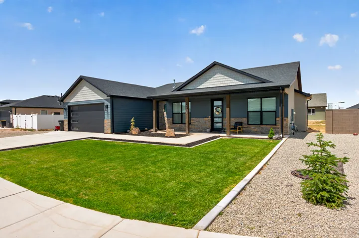 Modern ranch-style exterior with a covered porch, stone accents, dark siding, and a two-car garage